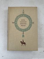 Front cover of the 1953 first edition Royal Canadian Mounted Police book showing compass design and mounted police figure.