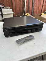 Top and front angle showing the Teac black 5-disc CD player and sealed remote control on white surface, unit has some dust.