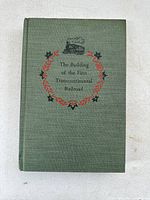 Top cover view of green cloth hardcover book with title and wreath design embossed in red and black.