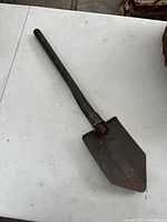 Full view of folding shovel showing blade and handle, surface rust visible.