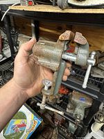 Side view of rusty clamp-on jeweler's vise being held in hand showing body, jaws, and clamp screw mechanism.