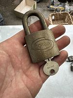 Photo of vintage Corbin brass padlock held in hand, showing front with embossed brand logo and key inserted.