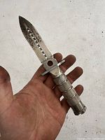 Photo showing full dagger inside a hand for scale, displaying knife blade with holes and metal handle.