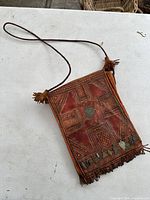 Front angled view of vintage handmade leather purse showing embossed geometric patterns, metal charms, and leather fringe