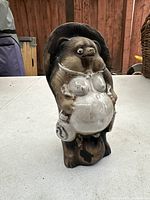 Full frontal view of vintage porcelain Tanuki raccoon dog statue with large belly and sake bottle.