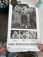 Full view of the poster showing the three main characters Curly, Moe, and Larry along with text and signatures, held by a hand to show scale.