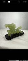Side view of natural ice jade horse figurine on wooden base showing detailed carving and translucence of jade.