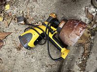 Side view of yellow and black Wagner electric paint sprayer showing paint container, trigger handle, and power cord on concrete ground with leaves.