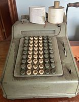 Front angled view of the National antique cash register showing the keys, paper rolls, and the crank handle.