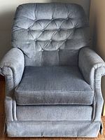 Front view photo of a blue comfortable armchair with tufted backrest, padded armrests, removable seat cushion, and skirted base.