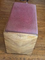 Rectangular wooden bedroom end stool with an upholstered cushioned seat in red-pink fabric showing wear and fading.