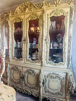 Front view of large ornate china cabinet hutch with glass doors and decorative carved woodwork topped with elaborate molding.