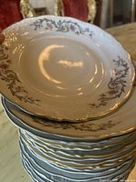 Stack of white china plates with scalloped edges, floral pattern in pink, purple, and green, and gold rim detailing.