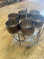 Photo of six silver-plated dessert glasses with frosted glass inside displayed on a wooden table, arranged in a cluster with a metal stand in front.