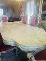 Close view of marble tabletop and ornate chair back showing gold-accented carvings and red velvet upholstery