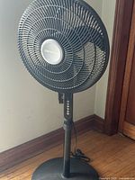 Front side view of Comfort Zone black floor fan showing the cage, blades, and control buttons on the stand.