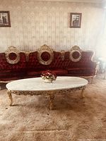 Front view of large velvet upholstered couch with oval marble coffee table in front, and floral arrangement on the table