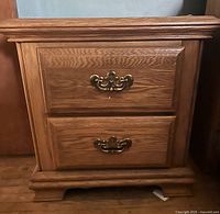 Front view of a man-made wood end table with two drawers, brass-tone handles, and carved short feet.