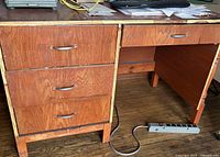 Photo showing front left side of wooden desk with 3 drawers stacked vertically, metal handles, and a shallow drawer on the right.