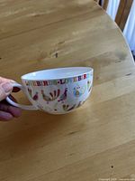 Photo of a white ceramic cup held in hand showing the love birds multicolor design around the exterior top rim.