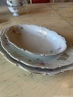 Photo of three porcelain serving dishes stacked together on a wooden table, showing floral decoration and gold accents