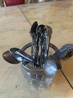Photo of a small set of silver spoons and forks with twisted, decorative handles held upright in a round glass holder with metal rim.