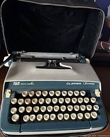 Photo of Smith Corona Clipper Courier manual typewriter with carrying case, showing front keyboard and case open behind it.