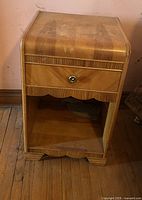 Wooden end table with drawer and lower shelf shown against a wall. Surface has marks and signs of wear.
