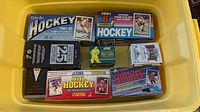 Overhead view of eight hockey card set boxes in yellow plastic bin.