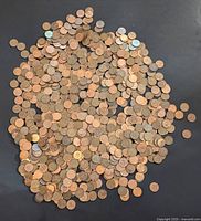 Wide view showing approximately 1000 pennies scattered on dark surface, majority copper colored with some green oxidation visible