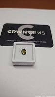 Oval cut chartreuse yellow green sapphire with blue undertones displayed in a white box with GRWN Gems branding in the background.