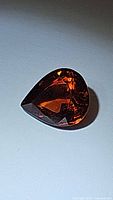 Photo of natural Spessartite garnet gemstone showing pear shape, deep orange color, multifaceted cut and clarity.