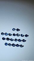 Top-down view of 24 round cut natural blue sapphires with deep cornflower blue color laid out on white background.