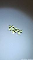 Ten small round, apple green natural Peridot cabochons placed on a white surface, showing size and color.