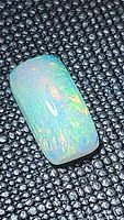 Close-up photo of a cushion cut Ethiopian opal with vibrant multicolored flash on a textured black surface.