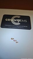 Three natural tourmaline gemstones ranging from champagne to padparadcha colors laid out below a GRWN Gems business card on a white background.