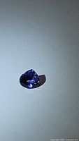 Photo of a single deep blue-purple pear-shaped tanzanite gemstone showing facets and clarity under light.