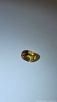 Close-up of the oval cut golden yellow Ceylon sapphire stone on a grey surface, showing color and clarity.