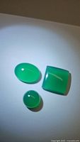 Three polished loose vivid green onyx gemstones displayed on white background under bright light, showing shape and color.