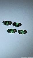 Four natural green oval cut tourmaline gemstones displayed on a white background under bright lighting, showing color and clarity.