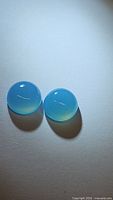 Pair of round blue chalcedony cabochons, smooth polished surface, translucent icy blue color, shown side by side on white background.