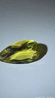 Photo of a pear cut lemon yellow citrine gemstone with facets visible, showing color and clarity under lighting.