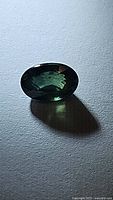 Close up photo of oval cut green blue sapphire gemstone casting shadow on flat surface