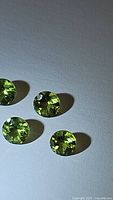Four round cut natural apple green Peridot gemstones arranged loosely on a white background, showing clarity and color.