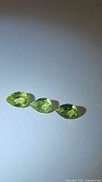 Three apple green pear cut peridot gemstones displayed on a white background to show shape, color and clarity.