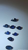 Photo of eight natural royal blue sapphire gemstones in a mix of oval and pear cuts, showing their deep royal blue color and polished surfaces.