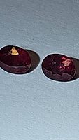 Close-up of two oval cut natural rubies with deep red coloration on white background showing shape and facets.