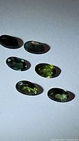 Six oval cut natural bright green sapphires arranged on a flat surface showing color and clarity.