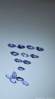 Photo of thirteen marquis cut natural tanzanite gemstones arranged on white background showing blue-violet hues and clarity.