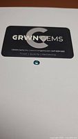 Natural oval cut teal aqua blue green topaz gemstone placed on white surface with brand card from GRWN Gems in background.